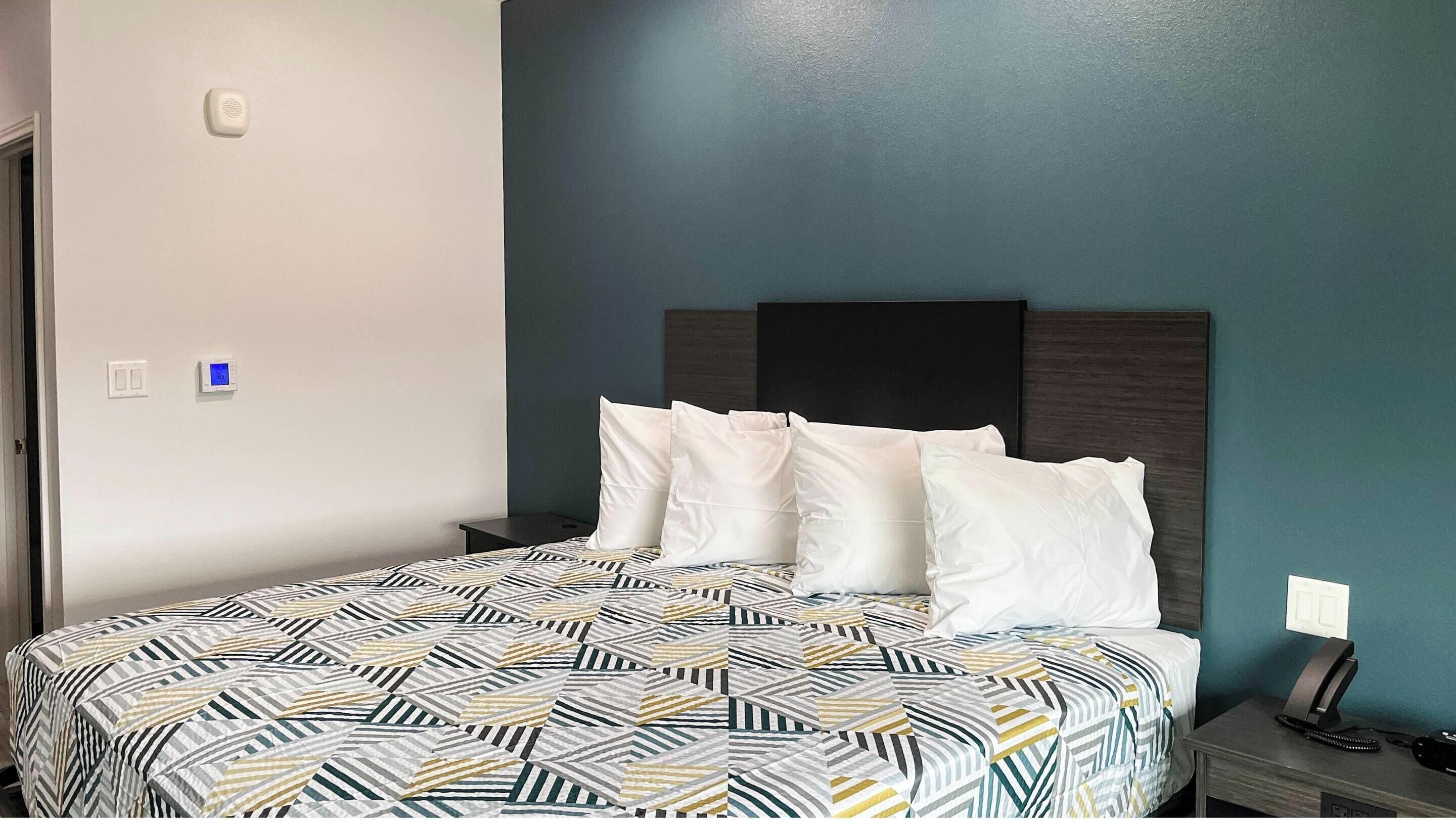 A neatly made bed with a patterned bedspread, a dark headboard, and a bedside table with a phone and a lamp.