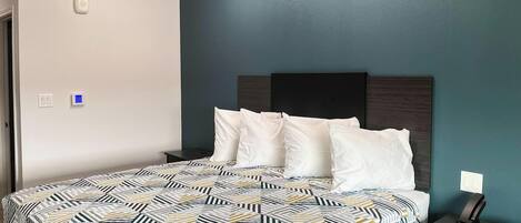 A neatly made bed with a patterned bedspread, a dark headboard, and a bedside table with a phone and a lamp.