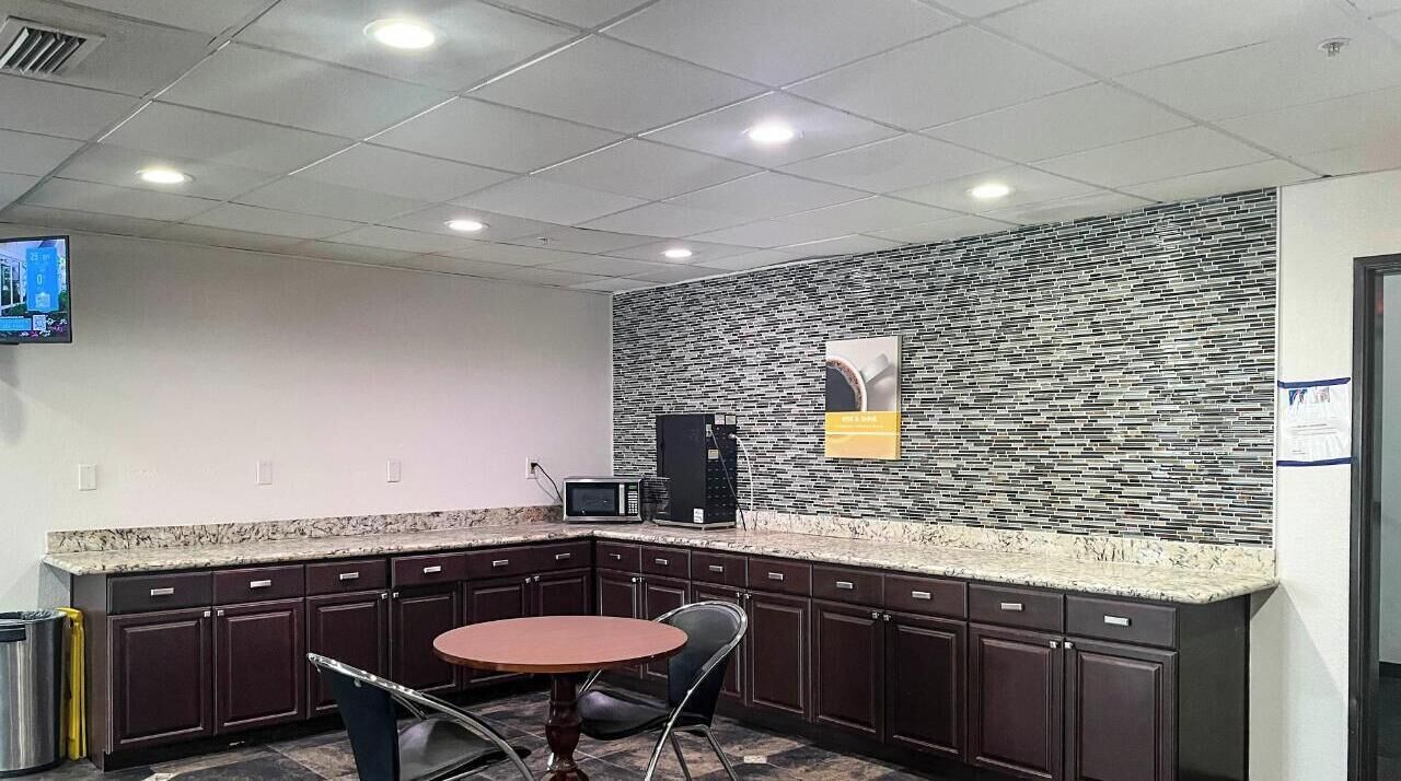 A modern kitchen with a granite countertop, dark cabinetry, a microwave, and a small table with chairs.
