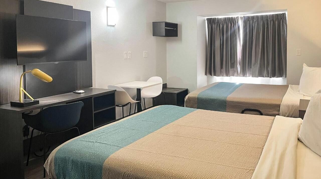 A hotel room with two beds, a desk, a chair, a TV, and a window with curtains.