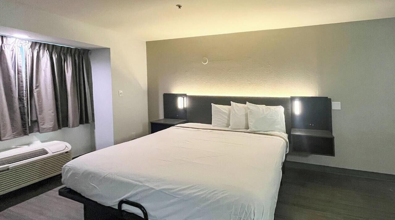 Een hotelkamer met een groot bed, een nachtkastje, een wandlamp en een raam met gordijnen.