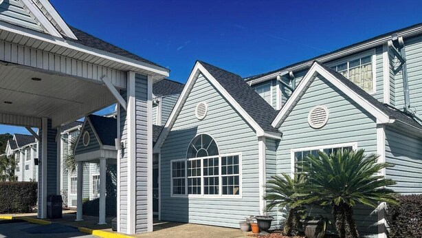 A light blue building with a covered entrance and large windows. - Studio 6 – Mobile, AL (Mobile)