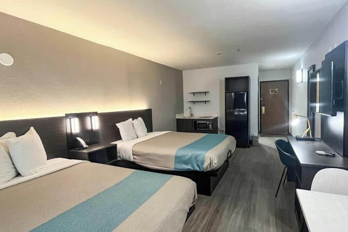 Ein Hotelzimmer mit zwei Betten, einem Schreibtisch, einem Sessel, einem Fernseher und einer Küchenzeile.