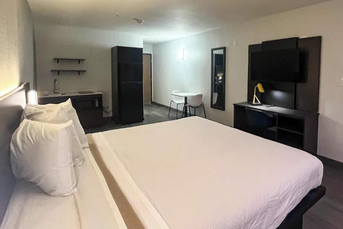 Ein Hotelzimmer mit einem großen Bett, einem Schreibtisch mit Stuhl, einem Fernseher und einer kleinen Küchenzeile.