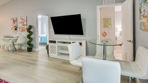 Un salon moderne doté d’un téléviseur à écran plat, de meubles blancs et d’une table en verre.