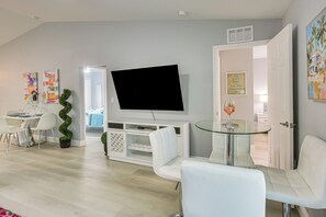 Ein modernes Wohnzimmer mit einem Flachbildfernseher, weißen Möbeln und einem Glastisch.