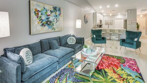 Un salon moderne avec un canapé bleu, des fauteuils turquoise et un tapis aux couleurs vives.