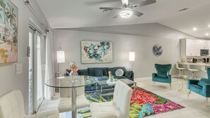 Un salon moderne avec une table basse en verre, un canapé, des fauteuils turquoise, un tapis coloré et un ventilateur de plafond.