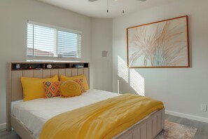 Un dormitorio con cama, una ventana con persianas, una obra de arte en la pared y una mesita de noche con lámpara.