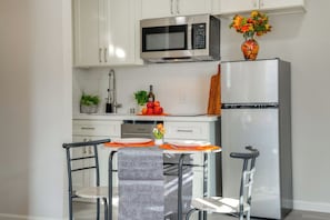 A modern kitchen with white cabinets, a stainless steel microwave, a refrigerator, and a dining area with a table set for two.
