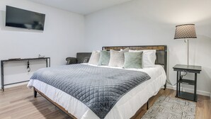 A modern bedroom with a large bed, a bedside table, a TV mounted on the wall, and a floor lamp. - Brand-New Sequim Escape: A/C, Fire Pit, Grill (Sequim)