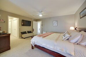 A bedroom with a bed, a ceiling fan, a TV, a bedside table, and a door leading to another room. - 3 Blocks to Lake George Village: Spacious Home! (Lake George)
