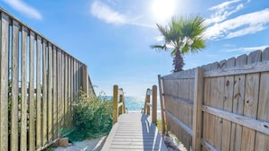Un sendero de madera que lleva a una playa con una palmera a la derecha.