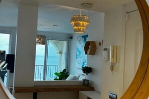 Ein Zimmer mit großem Fenster, einer Kristallleuchter, einer Pflanze und einer hölzernen Bank.