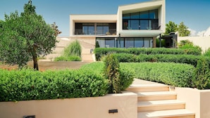 A modern two-story house with a flat roof, large windows, and a balcony. There are steps leading up to the entrance, surrounded by well-maintained hedges. - Luxury 4BR Seafront Villa with Pool and Jacuzzi (Sućuraj)
