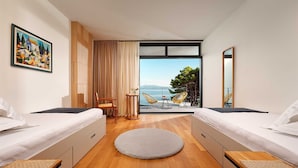 A modern hotel room with two beds, a round rug, a dining table with chairs, and a view of the sea. - Luxury 4BR Seafront Villa with Pool and Jacuzzi (Sućuraj)