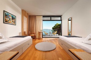 Una habitación de hotel moderna con dos camas, un tapete redondo, una mesa de comedor con sillas y vista al mar.