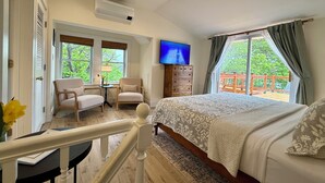 Une chambre avec un grand lit, une télévision, un bureau avec une lampe, deux chaises et une vue sur l’extérieur.