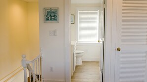 Un couloir doté d’un plancher en bois, de murs blancs, d’une porte blanche à panneaux ajourés et d’une rambarde blanche.