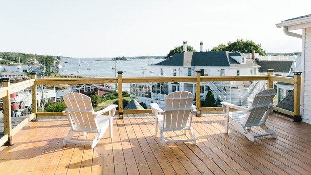 Une terrasse en bois avec deux chaises Adirondack blanches, disposées de manière à offrir une vue sur la mer et une île lointaine.