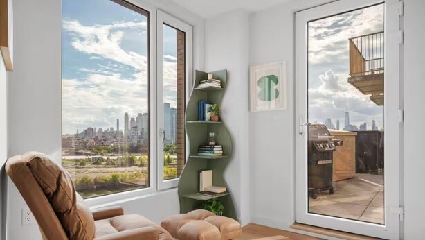 Uma sala de estar moderna com vista para a cidade, uma estante verde e uma poltrona de couro marrom.