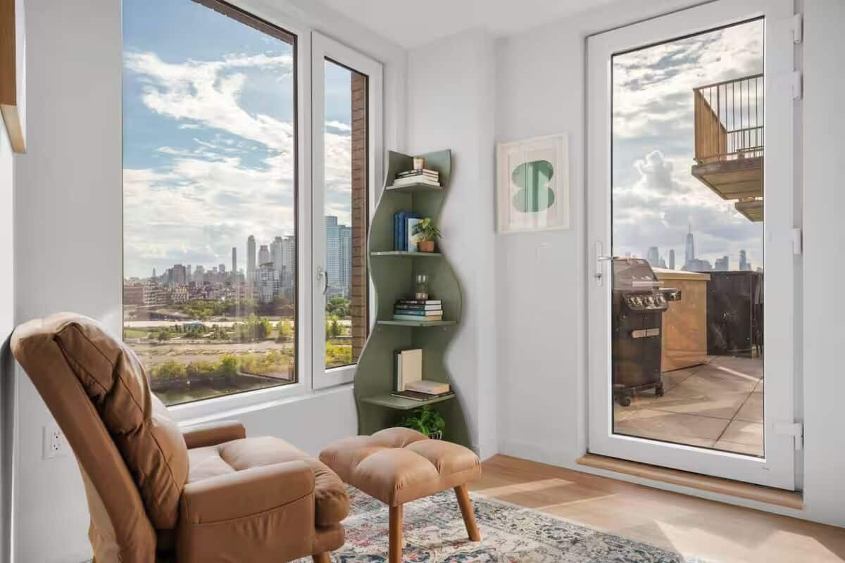 Uma sala de estar moderna com vista para a cidade, uma estante verde e uma poltrona de couro marrom.