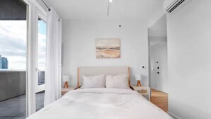 Quarto moderno com uma cama grande, vista para a cidade pela janela e um quadro na parede.