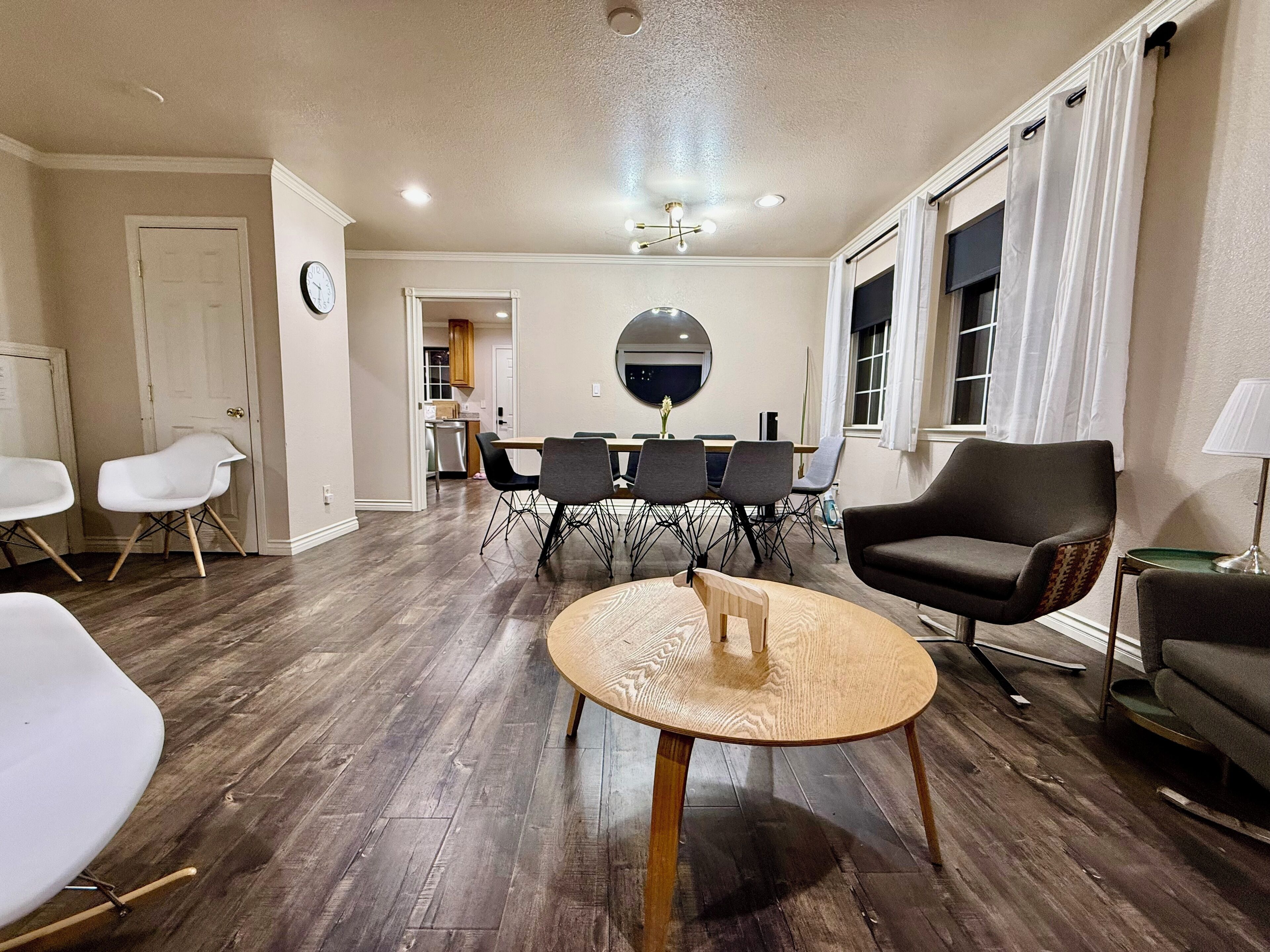 Un salon avec une table basse ronde en bois, un coin repas avec une table et des chaises, et une cuisine à l’arrière-plan.
