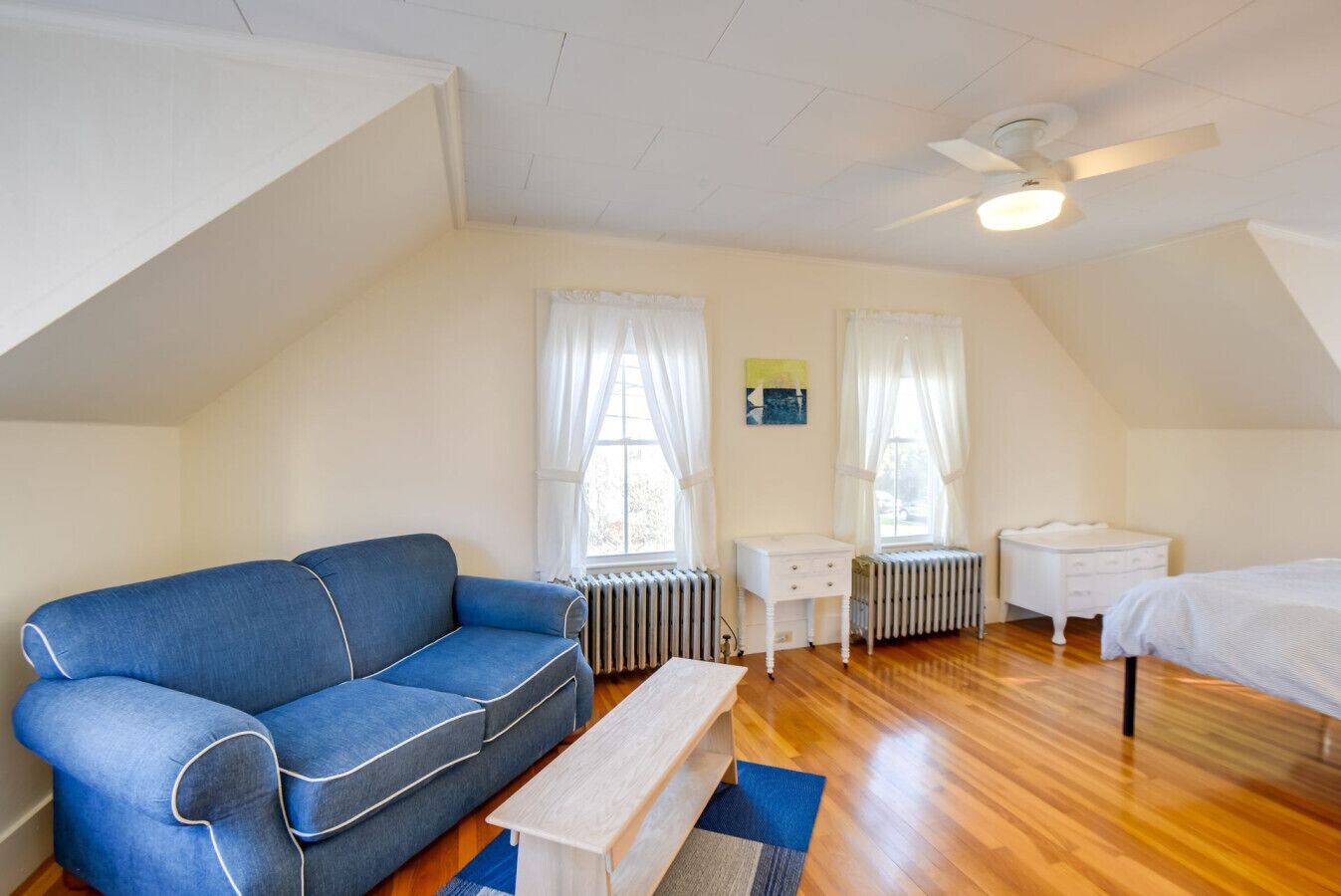 Une pièce avec un canapé bleu, une petite table blanche, un lit blanc et un radiateur.