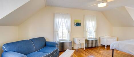 Une pièce avec un canapé bleu, une petite table blanche, un lit blanc et un radiateur.