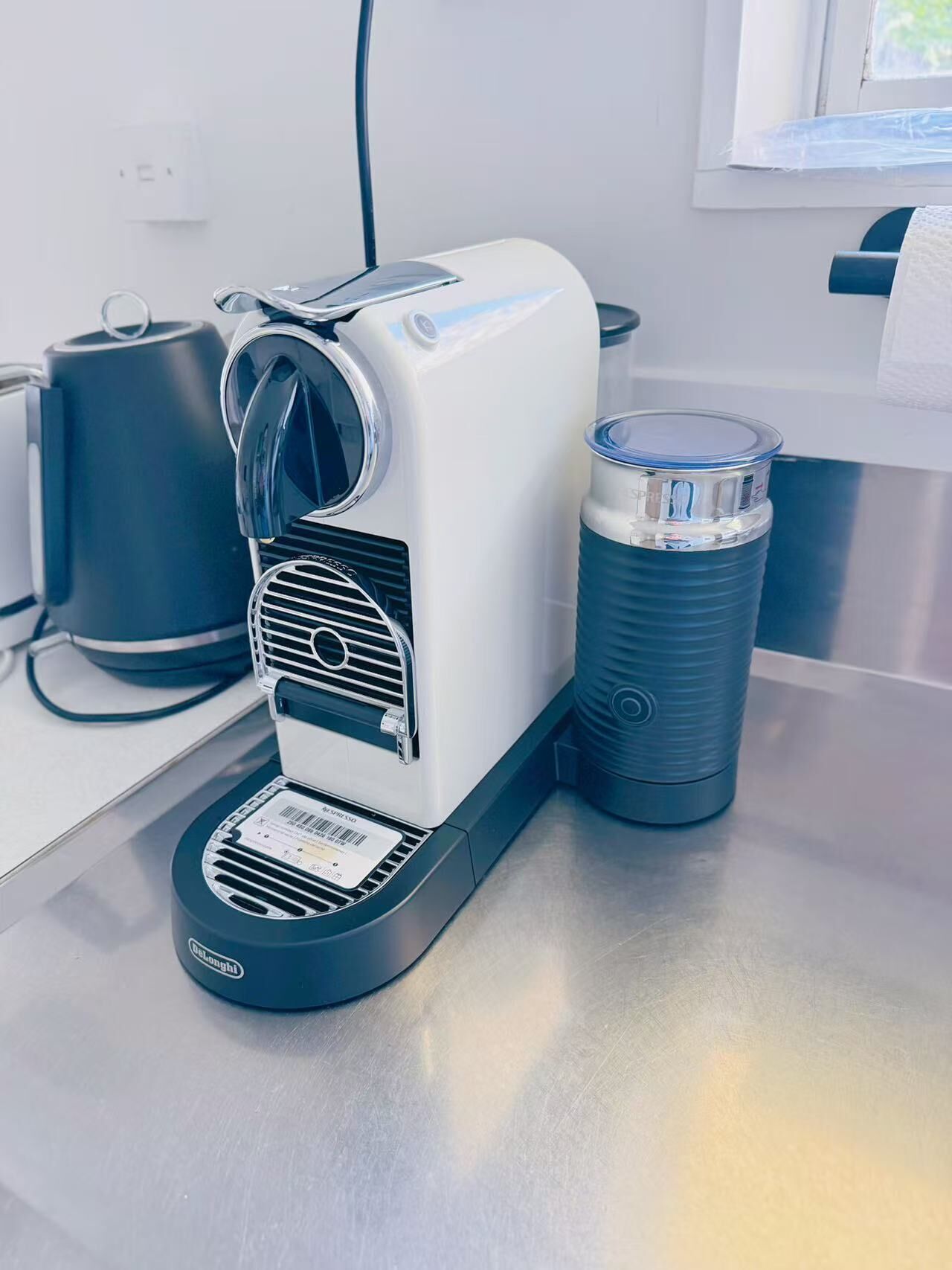 Une machine à café dotée d’un réservoir à eau et d’un récipient noir, le tout posé sur un plan de travail en acier inoxydable.