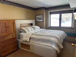 A bedroom with a bed, a wooden dresser, a window with a view, and a framed picture on the wall. - Ski In/Out condo close to everything with modern kitchen, balcony and views (Ludlow)