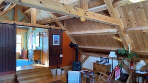 Interior rústico de madeira com teto alto, lareira, cadeira de balanço e tapete azul estampado.
