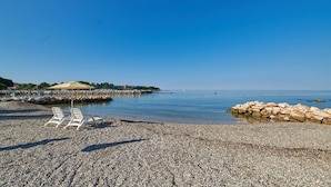 Ein Kiesstrand mit Liegestühlen und einer Steinmauer.