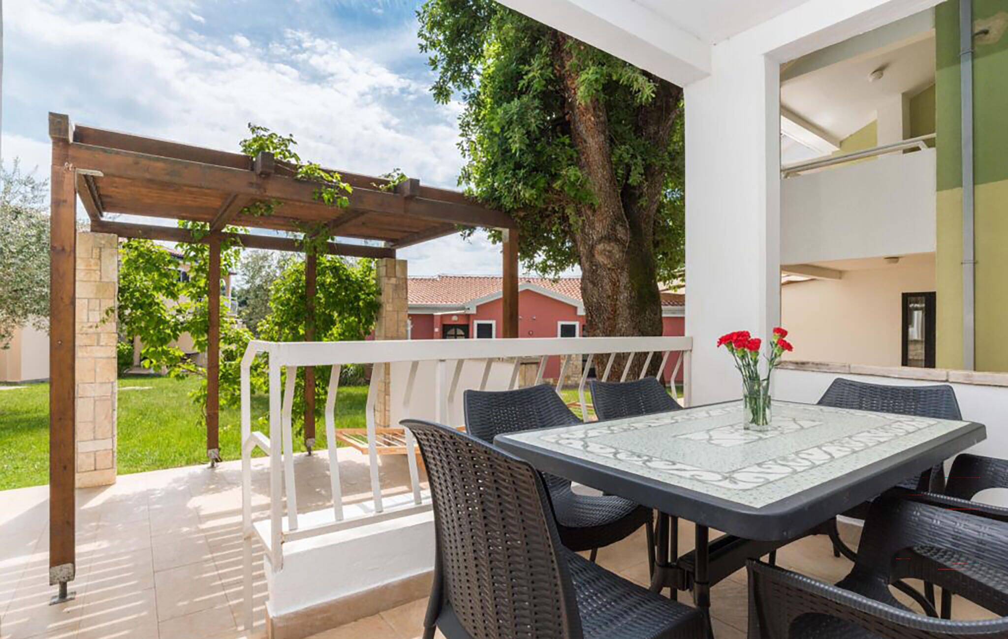 An outdoor patio with a table and chairs, a pergola, and a view of a residential area.