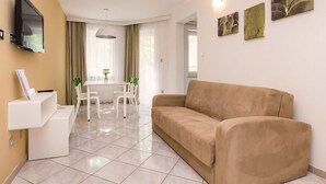 A living room with a beige sofa, a dining table with chairs, a TV mounted on the wall, and artwork on the wall. - Awesome apartment in Umag with swimming pool (Umag)