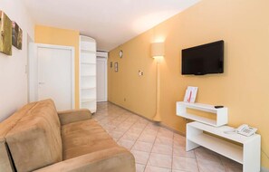Una sala de estar con un sofá, un televisor montado en la pared, una lámpara y una pequeña consola blanca con un teléfono.