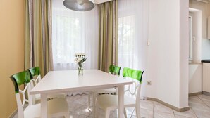 A dining area with a white table and chairs, a vase with flowers, and a view of a kitchen area. - Awesome apartment in Umag with swimming pool (Umag)