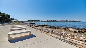 Un passeig marítim amb bancs de formigó, una barana metàl·lica i un límit de roca.
