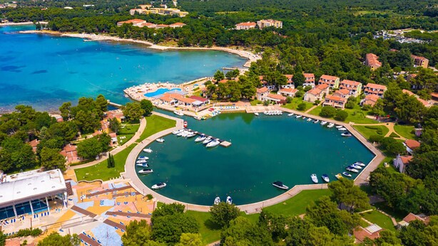 Vista aérea de un complejo turístico frente al mar, con un puerto deportivo, zonas verdes y edificios residenciales.