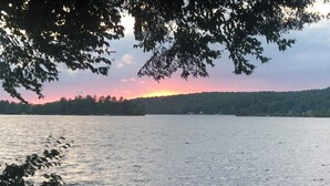 Un lago tranquillo con un tramonto sullo sfondo e alberi in primo piano.