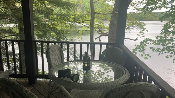 Una terrazza con sedie in vimini e un tavolo in vetro che si affaccia su un lago.