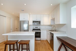 A modern kitchen with white cabinetry, stainless steel appliances, and a wooden bench. - Premier Oceanfront Luxury in Oak Bay South (Oak Bay South)