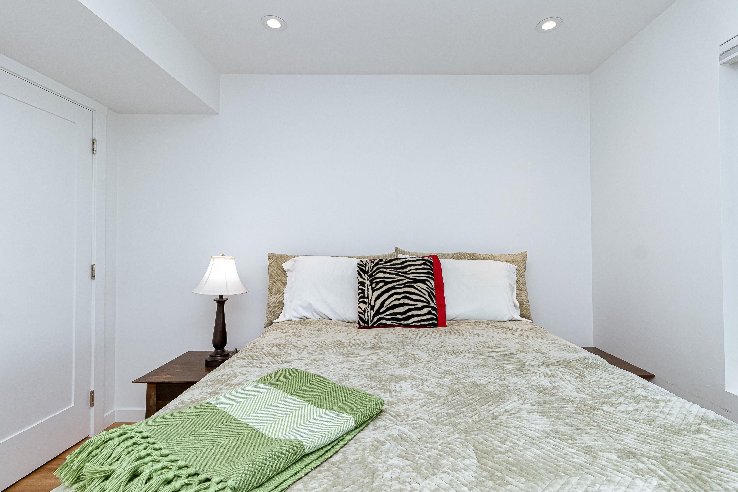 Een slaapkamer met een bed, nachtkastje, lamp en raam.