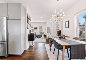 A modern kitchen with a dining area, wooden flooring, and a large window. - Luxury Boston Base · 2 Suites · 2 Baths · Red Line · Parking · Davis Square (Somerville)