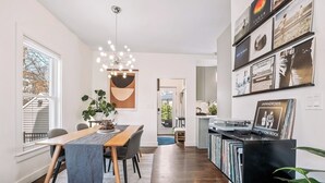 Eine moderne Küche mit integriertem CD-Regal, einem Essbereich mit Holztisch und -stühlen sowie einem großen Fenster mit Jalousien.