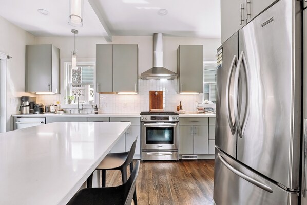 A modern kitchen with stainless steel appliances, a central island, and light-colored cabinetry. - Luxury Boston Base · 2 Suites · 2 Baths · Red Line · Parking · Davis Square (Somerville)