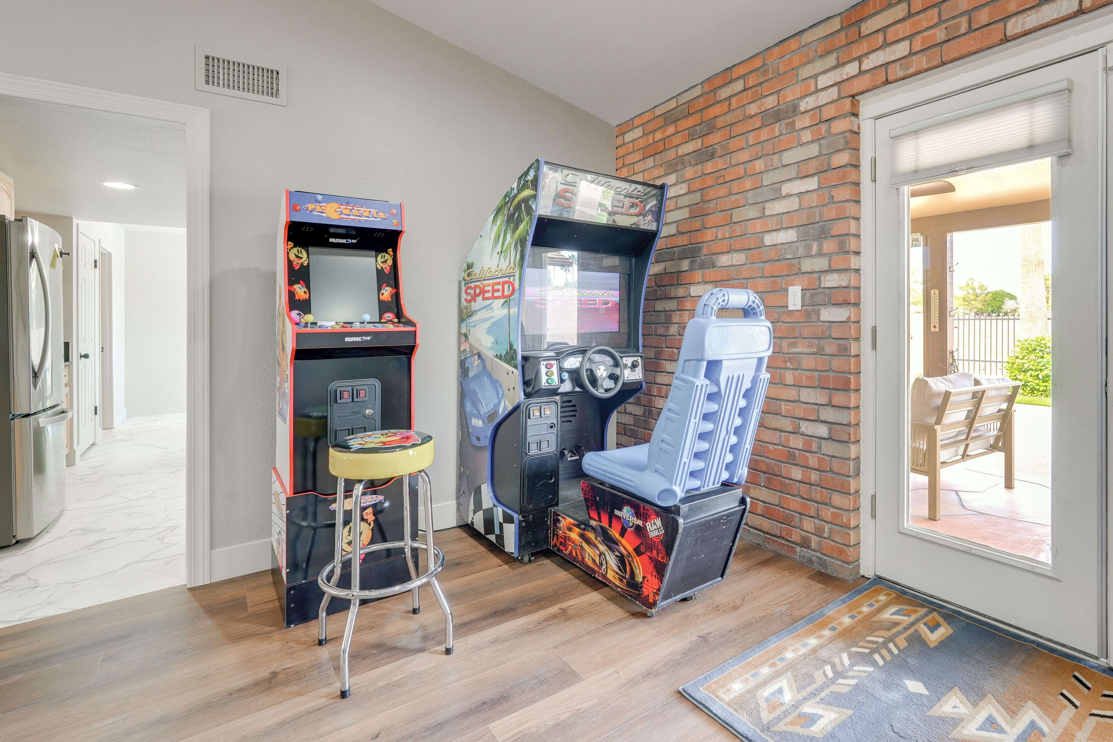 A room with two arcade machines, a small stool, and a door leading to an outdoor area.