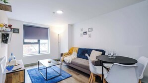 Uma sala de estar moderna com sofá, mesa de centro, mesa de jantar com cadeiras, uma janela grande e um abajur.
