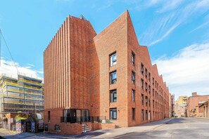 A modern brick building with a unique angular design, featuring multiple windows and a visible entrance. - Central Liverpool Apartment | Work & Long Stays (Merseyside)